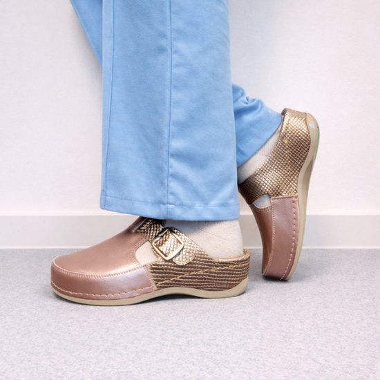 Voeten in roze metallic klompen met slangenhuid-achtig detail, gedragen met een blauwe broek.