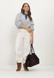 Model in grijze crop sweater, witte broek, bruine laarzen en een grote donkere suède tas.