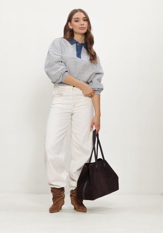 Model in grijze crop sweater, witte broek, bruine laarzen en een grote donkere suède tas.