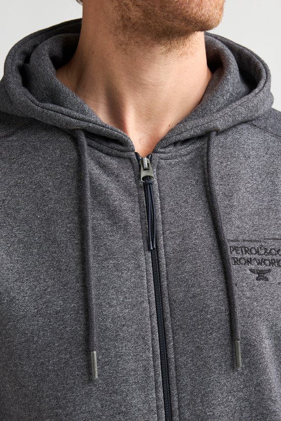 Close-up van het grijze vest met rits, trekkoorden en "PETROL&CO IRON WORKS"-logo op de borst.