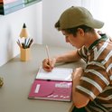 Jongen in gestreept shirt tekent op een Kidywolf-tekenbord aan een bureau met een pennenhouder in potloodvorm.