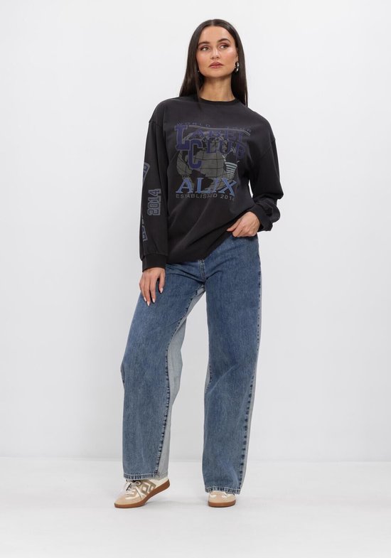 Vrouw in lang T-shirt met 'Label Club World Tour' print, globe en 'ALIX' in donkere tinten, met blauwe jeans.