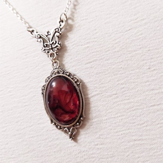 Donkerrode ovale hanger aan een zilverkleurige ketting met sierlijke filigraan rand.