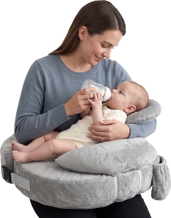 Vrouw voedt baby met fles, ondersteund door een grijs voedingskussen.