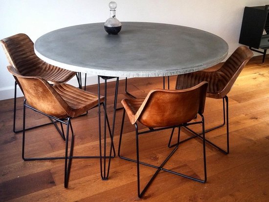 Ronde betonnen eettafel met vier bruin lederen kuipstoelen met zwarte metalen poten.