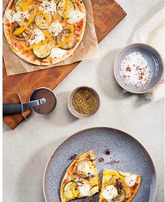 Vegetarische pizza met courgette, aubergine en paprika, geserveerd op een bord met kruiden en zout.