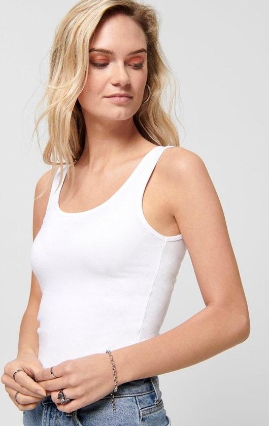 Close-up van een vrouw met een witte tanktop met spaghettibandjes, spijkerbroek en ringen.