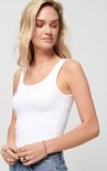 Close-up van een vrouw met een witte tanktop met spaghettibandjes, spijkerbroek en ringen.