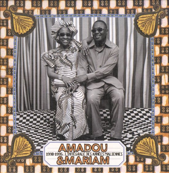 Een man en vrouw zitten naast elkaar, met op de achtergrond een gestreept gordijn. De vrouw draagt een hoofddoek en een jurk met grafische patronen. Ze heten Amadou & Mariam.