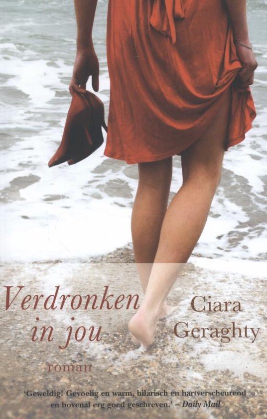 Een vrouw in een oranje jurk staat op het strand, met de zee op de achtergrond. Ze draagt een schoen in haar hand.