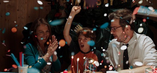 Een gezin viert een verjaardag met confetti en een taart.