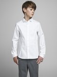Garçon portant une chemise blanche à manches longues avec des boutons blancs et un pantalon gris.