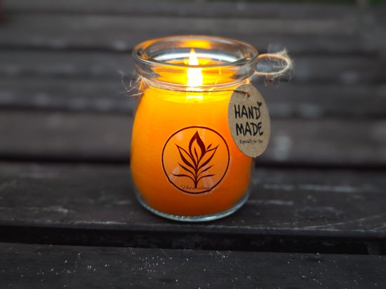 Brandende oranje bijenwaskaars in een glazen pot met een "HAND MADE" label en een bruin logo.
