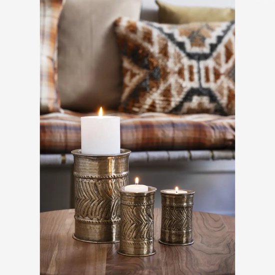 Drie bronzen kandelaars met reliëfpatroon, met brandende witte kaarsen, op een houten tafel.