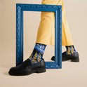 Model draagt gele broek, zwarte loafers en sokken met Van Goghs Sterrennacht.