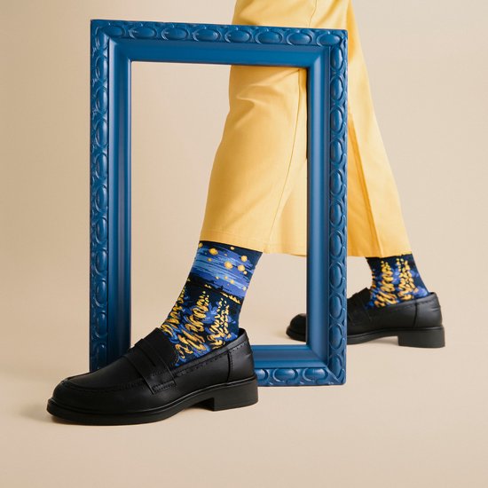 Model draagt gele broek, zwarte loafers en sokken met Van Goghs Sterrennacht.