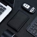 Zwarte lederen pasjeshouder op een zwarte ondergrond, naast een laptop, toetsenbord en autosleutel.