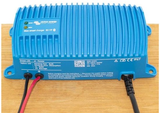 Blauwe Victron acculader op houten ondergrond met rode, zwarte draden en zwarte kabel.