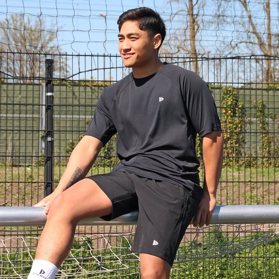Man in zwart Donnay T-shirt en zwarte short, zittend op een hek.