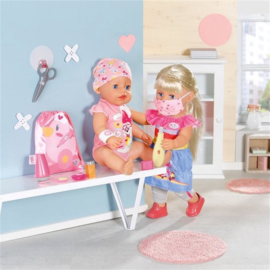 Een baby Born pop met masker en roze outfit wordt verzorgd door een andere pop met masker.