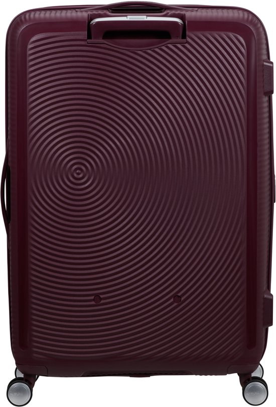 Burgondische koffer met cirkelvormig patroon, handvat aan de bovenzijde en vier wielen. 'American Tourister' logo op de voorkant.