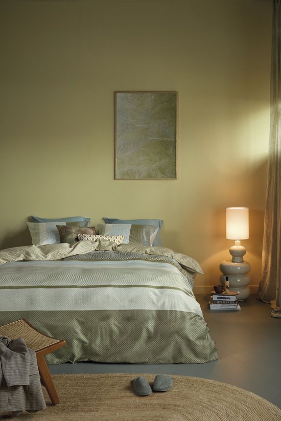 Lit fait avec une housse de couette verte à rayures, dans une pièce aux murs jaunes avec une lampe sur pied.
