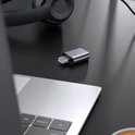 Grijze QOST USB geluidskaart adapter op een bureau naast een laptop.