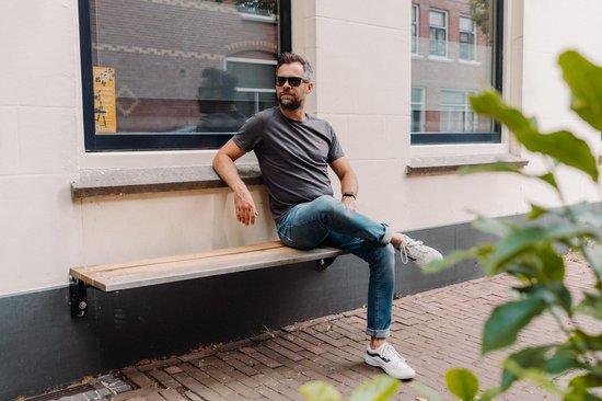 Man met zonnebril zit op houten gevelbank met jeans en grijs shirt.