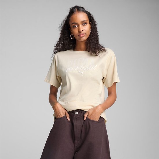Model draagt een lichtbeige PUMA T-shirt met 'PUMA Sports Club' logo en donkere broek.