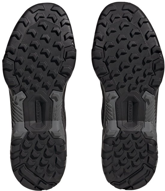 De onderkanten van twee zwarte wandelschoenen met een robuust profiel en 'TRAXION' op de zool.