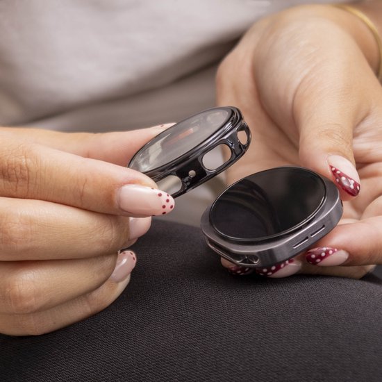 Twee delen van een zwarte smartwatch beschermhoes worden vastgehouden. De handen hebben nagellak met rode stippen.