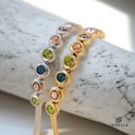 Goudkleurige en zilverkleurige armbanden dichtbij elkaar, elk met een rij veelkleurige edelstenen.