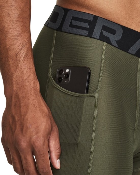 Detail van de olijfgroene Under Armour sportlegging met zijvak waarin een zwarte smartphone zit.