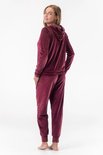 Model in bordeauxrood fluwelen joggingpak, achterkant: capuchonvest met rits en joggingbroek.