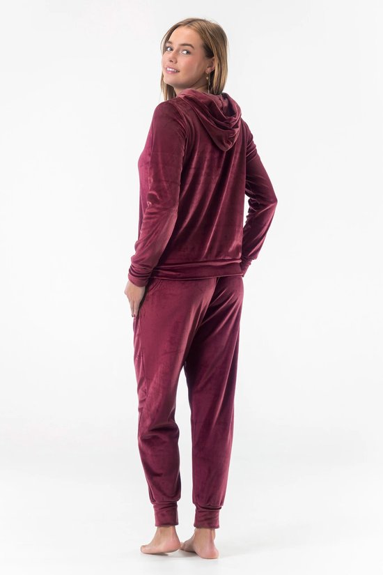 Model in bordeauxrood fluwelen joggingpak, achterkant: capuchonvest met rits en joggingbroek.