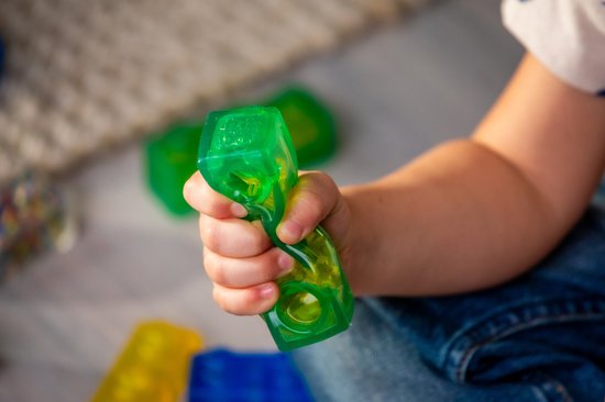 Kind knijpt in een groene, transparante Jelly Blox bal gevuld met gekleurde bolletjes.