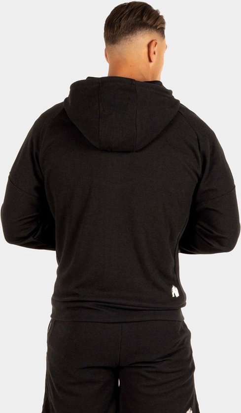 Man met spierbundel, achterkant van een zwarte trainingsjas en korte broek van Gorilla Wear.