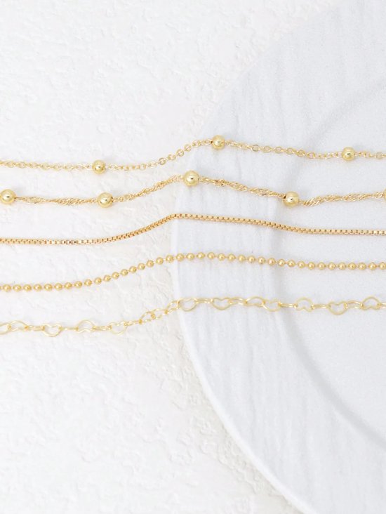 Vijf gouden armbandjes met diverse schakels en gouden kraaltjes, op een witte ondergrond.