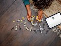 Mains d'enfant construisant un AT-RT walker LEGO Star Wars avec des pièces jaunes et grises, à côté de petites figurines LEGO et d'une tablette.