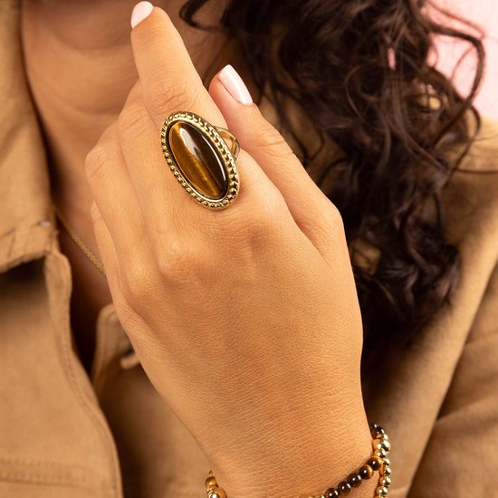 Model draagt een gouden ring met een ovaal tijgeroog en een gouden armband met bruine en gouden kralen.