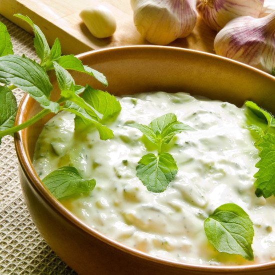 Schotel met romige tzatziki, gegarneerd met verse muntblaadjes. Knoflook en komkommer zichtbaar.