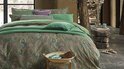 Gedrapeerd bed met meerdere groene kussens en een dekbedovertrek met paisley print.