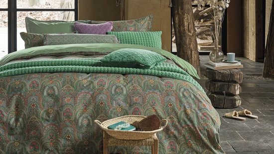 Gedrapeerd bed met meerdere groene kussens en een dekbedovertrek met paisley print.