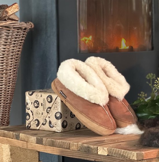 Bruine schapenvacht sloffen met witte wollen voering op een houten tafel.