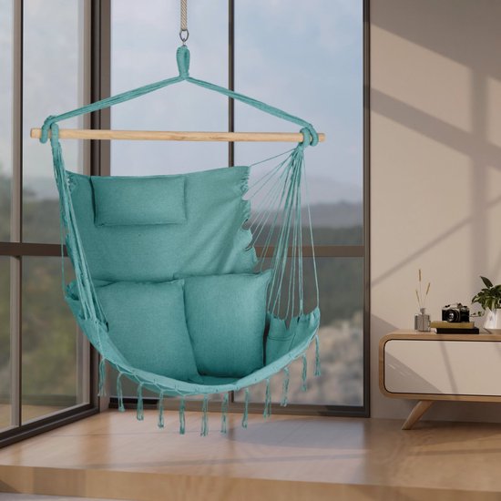 Turquoise hangstoel met 3 kussens en franjes, hangend bij een groot raam met uitzicht op de bergen.