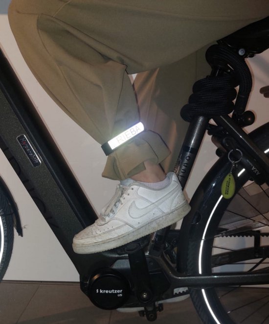 Zwarte broekklem met reflecterend 'RIEBA' logo om de enkel van een persoon die op een fiets zit.