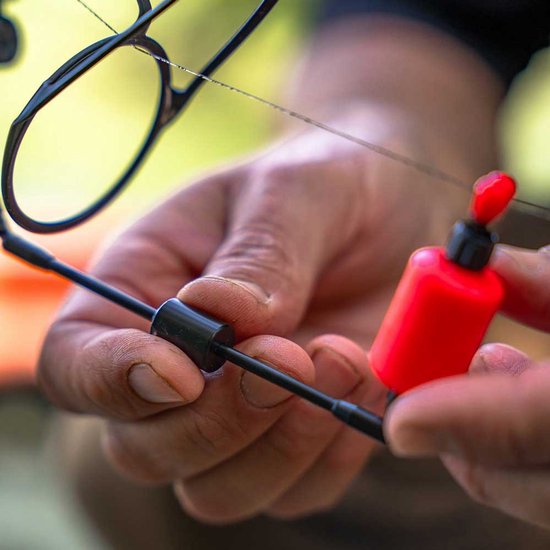 Mains ajustant un swinger de canne à pêche rouge avec un bras noir et une fixation noire.