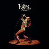 Albumhoes: Wolf Alice - The Clearing. Een zangeres in een glinsterend groen pak, rode riem en bruine laarzen.