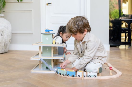 Houten speelgoedgarage met trein en kinderen, groen met houten details.