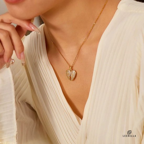 Close-up van een vrouw met een gouden ketting met een hartvormige vleugel hanger met steentjes.